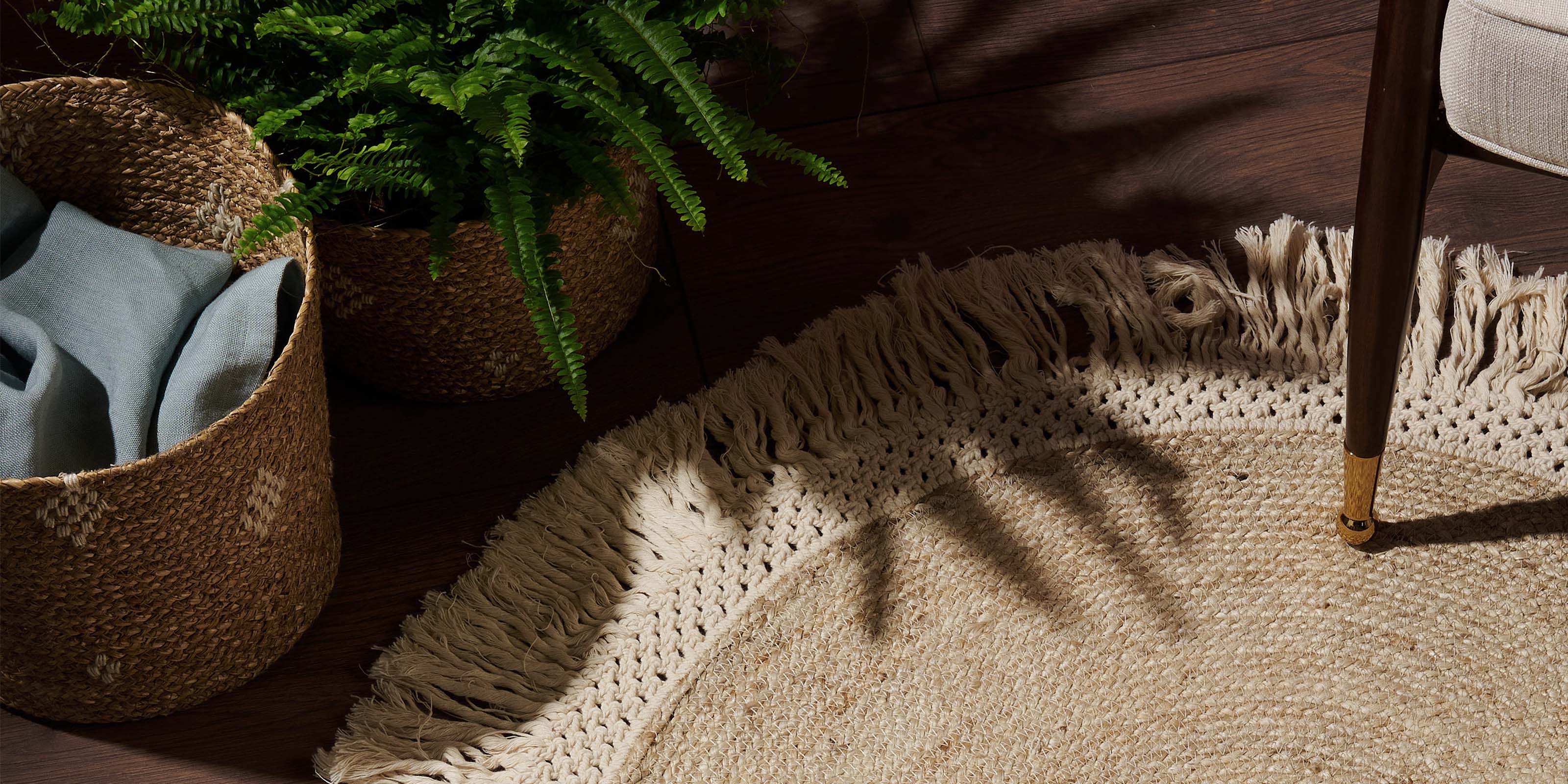 Handmade jute and macrame rug on a wooden floor next to handmade baskets, with an armchair