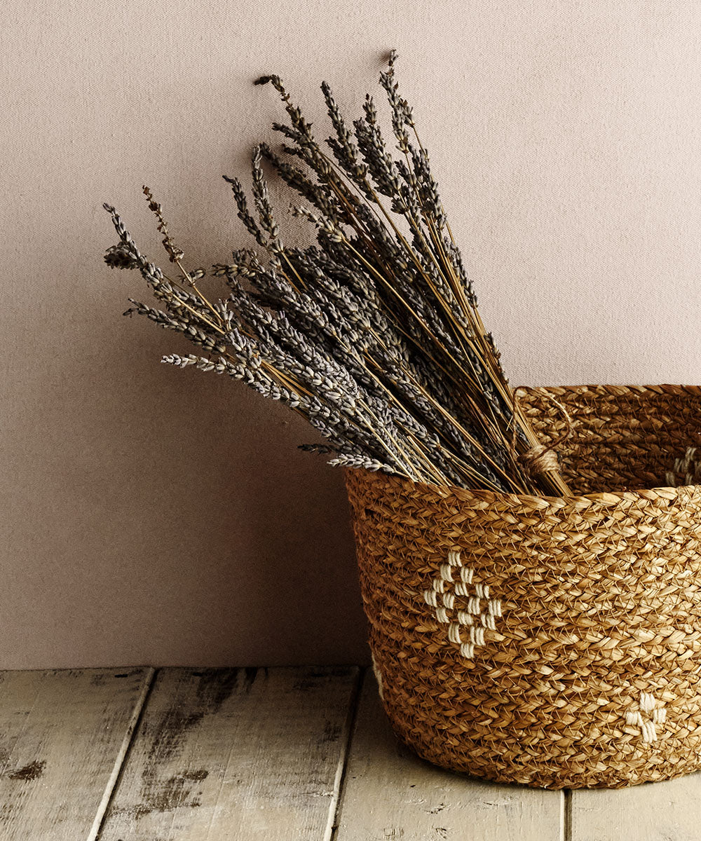 Handmade jute and cotton basket on a wooden floor, against a wall, with a bunch of lavender inside