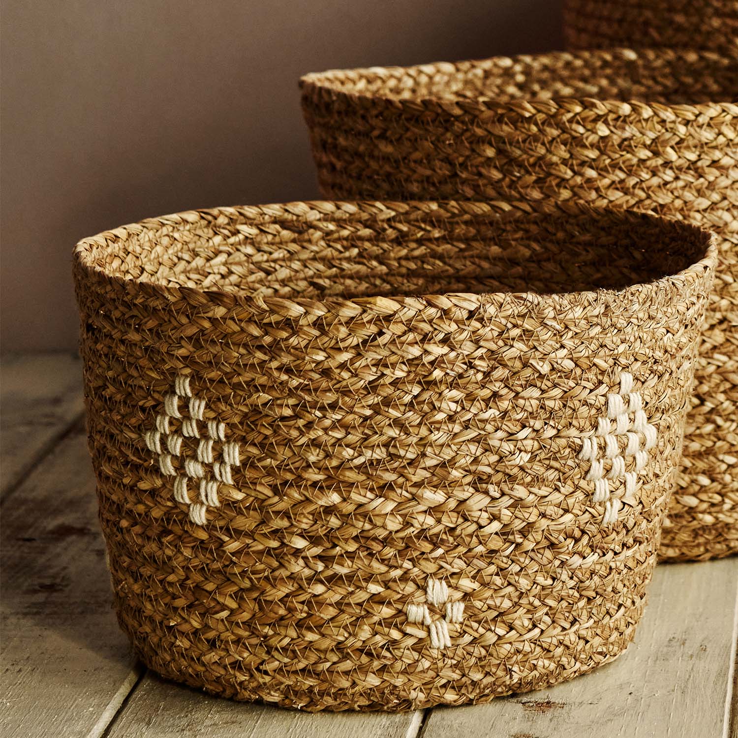 A small handmade basket made of jute and cotton, on a wooden floor, with a larger one behind