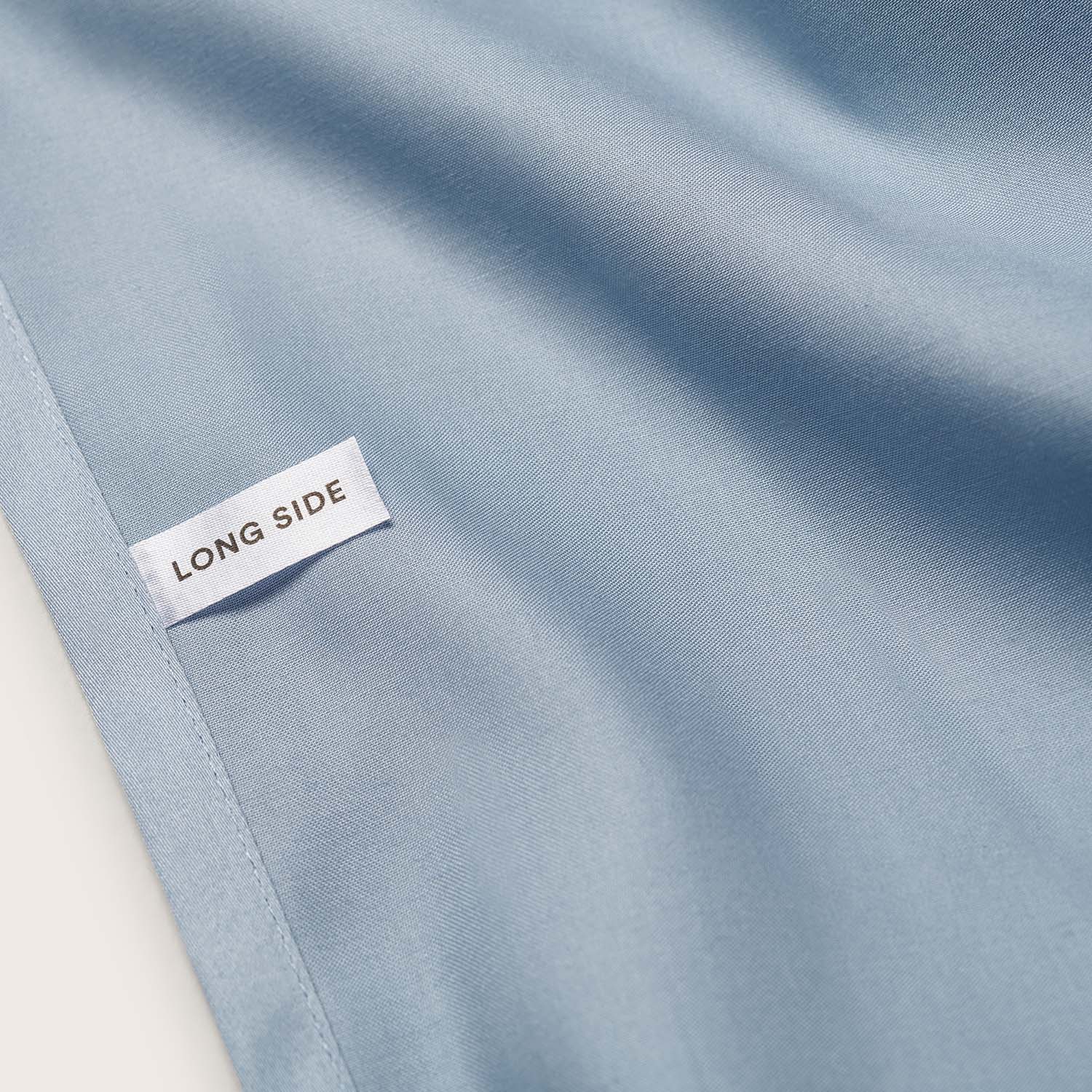 Close up of blue sateen fitted sheet with a label for the long side