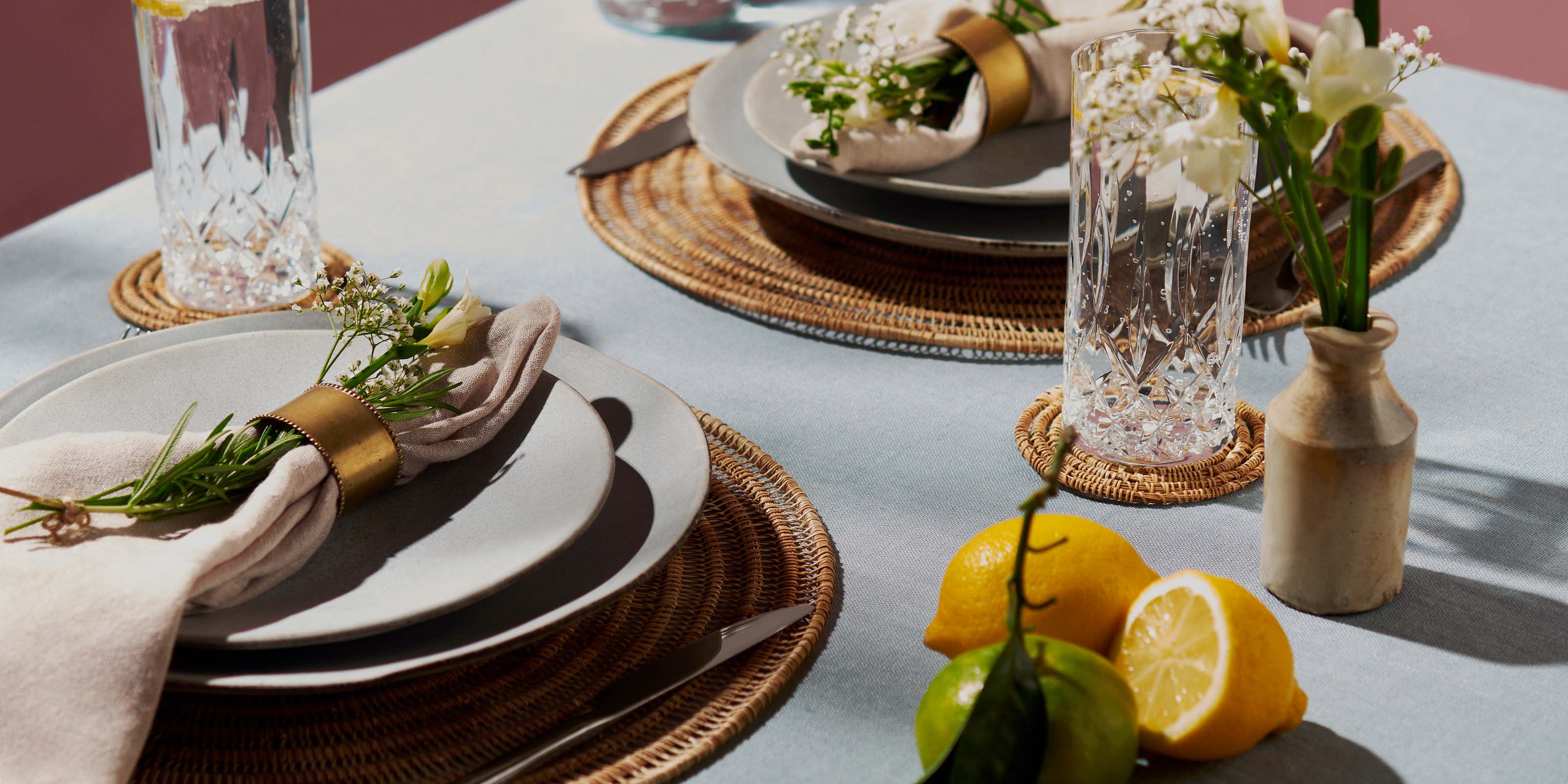 Table setting with handmade placemats and coasters, freshly cut lemons and a lime, crystal glasses, napkins and flowers